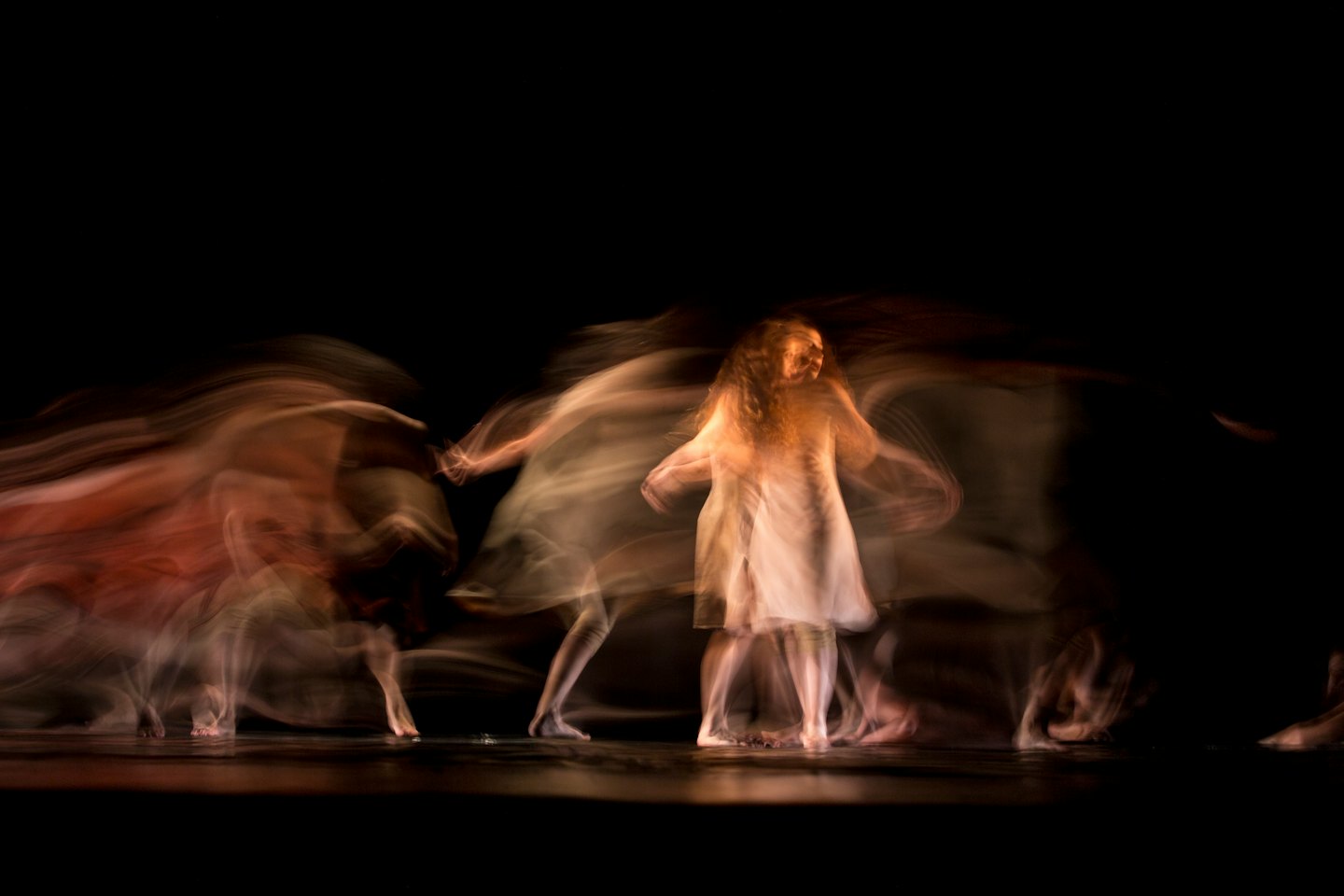 Dancers in flowing costumes move across a dark stage.