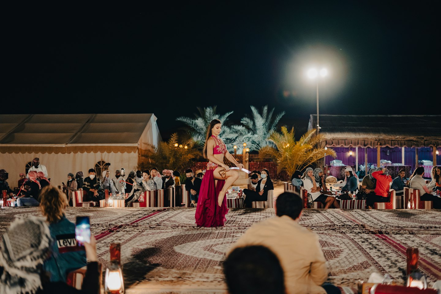 Belly dancer performs on a platform for an audience outdoors.