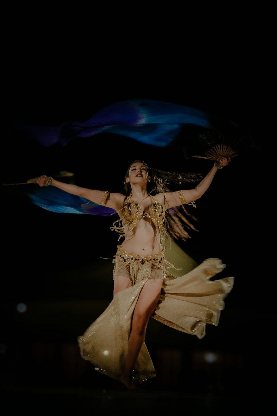 Woman performs belly dance in ornate costume with silk flag.