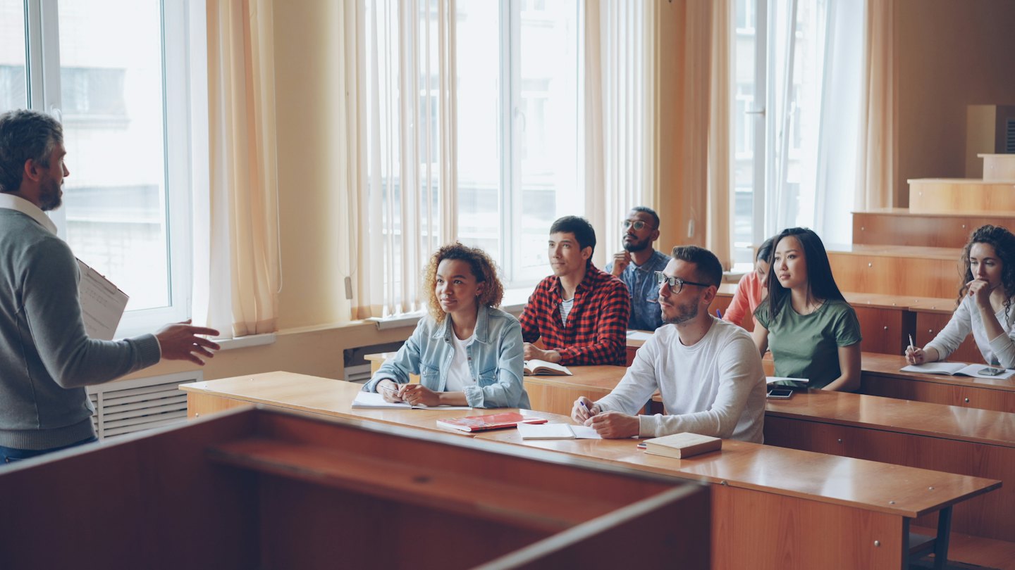 Instructor lectures diverse young adults in a bright classroom.