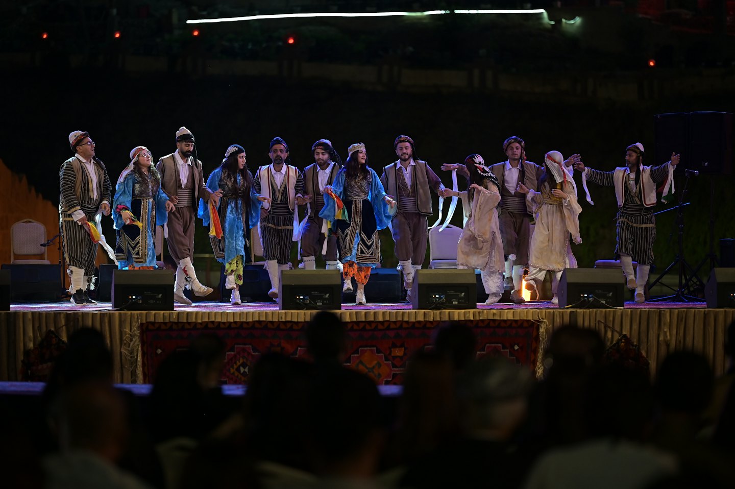 Performers in traditional costumes dance on an outdoor stage.